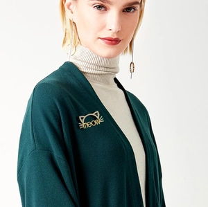 Détail d'une broche chat dorée meow et de boucles d'oreilles géométriques sur un mannequin