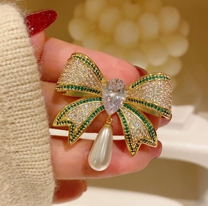 Macro shot of bow brooch with green crystals and a teardrop pearl on clothing