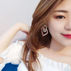 Detail of model wearing double-layered geometric heart earrings with pink rhinestones