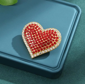 Detailed macro shot of red heart rhinestone brooch with gold base and white crystal trim