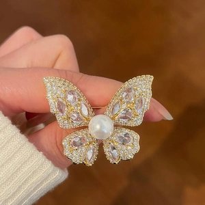 Sparkling butterfly brooch with clear crystals and a central white pearl in gold finish