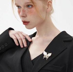 Detalle de un elegante broche de mariposa dorado con perlas sobre solapa negra