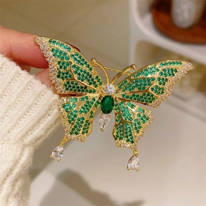 Macro detail of emerald butterfly brooch with green gems and zircons on white knit sweater