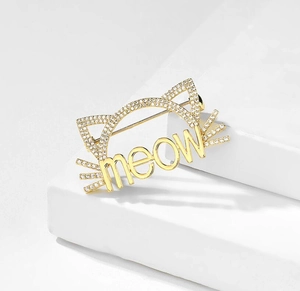 Gros plan sur la broche chat dorée avec lettrage meow scintillant et oreilles en zircon