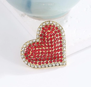 Macro detail of gold alloy heart brooch with red and white rhinestones on textured stone