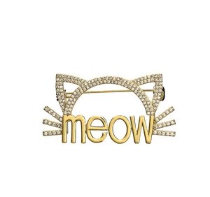 Détail d'une broche chat dorée avec zircons micro-pavés et gravure meow sur fond blanc pur
