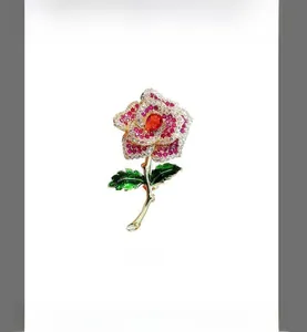 Detailed macro of golden rose brooch with red crystals and green enamel leaves