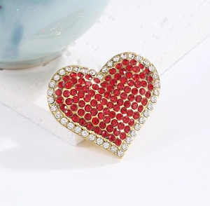 Macro detail of red heart brooch with crystal edges and golden alloy base on white stand
