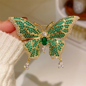 Macro shot of gold-plated butterfly brooch with emerald main stone and green zircons