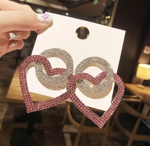 Detailed view of oversized silver stud earrings with sparkling pink crystal heart pendants