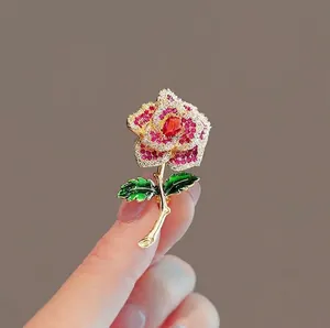 Exquisite handmade gold flower brooch with red crystals and green leaves shown on hand