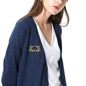 Détail d'une broche chat dorée avec texte meow sur un pull en maille bleu foncé