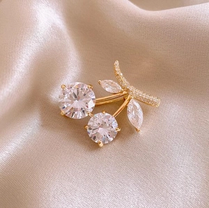 Exquisite gold cherry brooch with transparent zircon crystals on champagne silk background