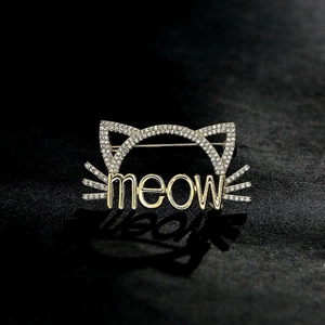 Détail d'une broche chat dorée sertie de cristaux blancs avec inscription meow