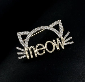 Détail de la broche dorée meow ornée de strass brillants sur un fond en velours noir
