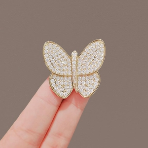 Detail of a gold butterfly brooch with shimmering rhinestones held on fingertips