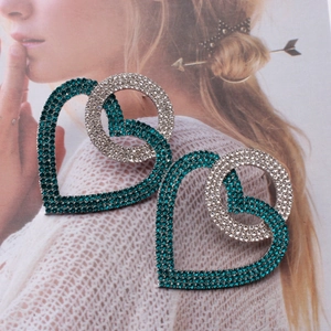 Detail view of large heart-shaped crystal earrings with emerald and white rhinestones