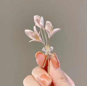 Détail de la broche fleur de lys rose avec pétales dorés et nœud en zircon brillant