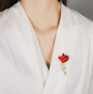 Détail d'une broche fleur rouge mat avec cristal et perle sur une blouse en soie blanche