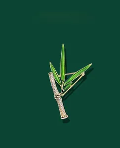 Dettaglio spilla in bambù con finitura oro, foglie in smalto verde e cristalli