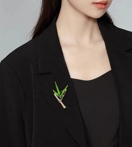 Dettaglio della spilla a forma di bambù in smalto verde su revers di blazer nero