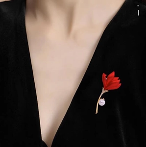 Gros plan sur une élégante broche fleur rouge avec tige dorée et perle sur vêtement noir