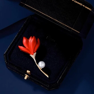 Détail macro d'une broche tulipe rouge avec tige dorée et perle dans un écrin bleu