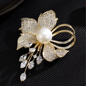 Élégante broche fleur avec perle, cristaux scintillants et pompons dorés sur fond noir
