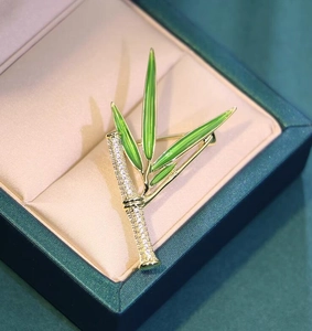 Dettaglio spilla in bambù dorato con smalto verde e zirconi lucidi su confezione