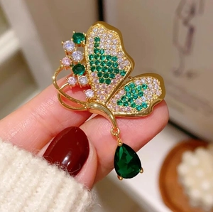 Elegante spilla a farfalla dorata con cristalli verde smeraldo e ali pavé scintillanti