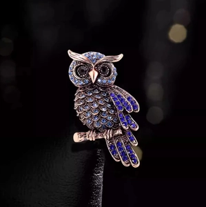 Macro detail of blue crystal encrusted owl brooch on rose gold branch accessory