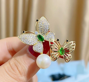 Makro-Detail der goldenen Schmetterlingsbrosche mit grünen Steinen, Zirkonen und Perle