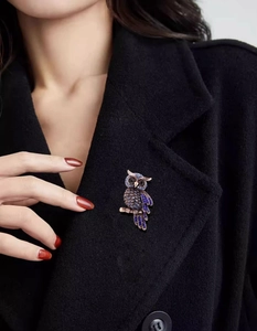 Detailed view of luxury blue rhinestone owl brooch pinned on black wool coat collar