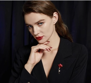 Broche fleur rouge élégante avec tige dorée et perle sur le revers d'un blazer noir