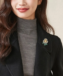 Détail d'une broche camélia élégante avec pierre jaune et strass pavés sur manteau noir
