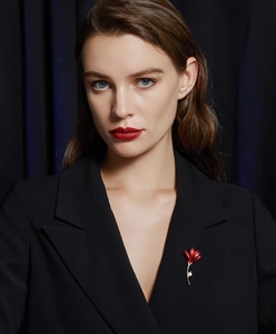 Détail d'une broche fleur rouge avec tige dorée et perle sur un revers de blazer