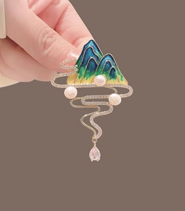 Macro detail of landscape brooch with blue enamel mountains, pearls and gold tassels