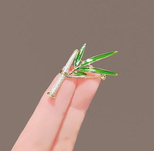 Dettaglio macro della spilla bambù con cristalli scintillanti e foglie in smalto verde
