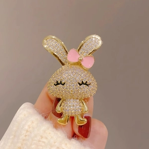 Vue détaillée d'une broche lapin dorée ornée de strass brillants et d'un nœud rose