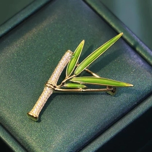 Elegante spilla a bambù dorata con cristalli e smalto verde su una scatola per gioielli