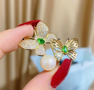 Details von grünen Marquise-Steinen, Schmetterlingsflügeln und Perle auf Goldbrosche