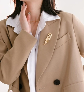 Vue détaillée d'une broche plume dorée avec perle blanche sur le revers d'un blazer