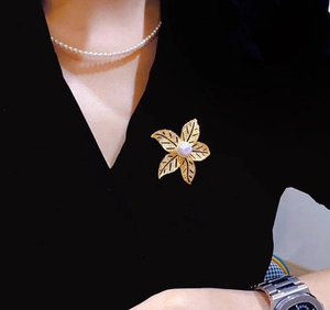 Détail d'une broche feuille dorée avec perle blanche sur un haut élégant à col en V