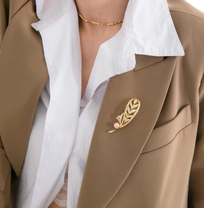 Détail d'une broche feuille dorée ajourée avec perle et cristaux sur le revers d'une veste