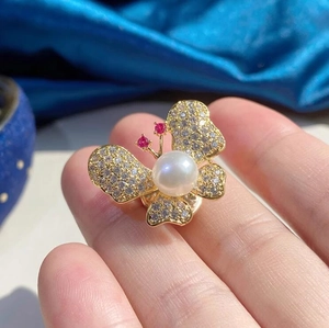 Élégante broche papillon dorée avec cristaux scintillants et une perle blanche centrale