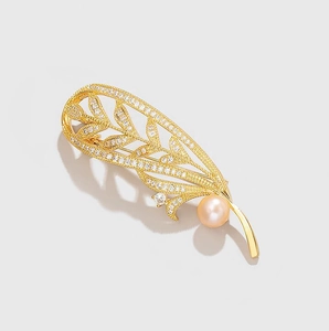 Détail macro d'une broche plume dorée sertie de zircons et d'une perle rose délicate