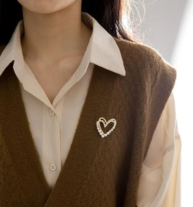 Détail d'une broche cœur dorée avec perles fixée sur un gilet en maille marron