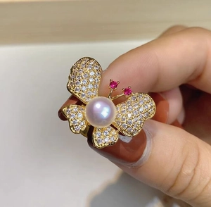 Détail d'une broche papillon dorée avec perle blanche et touches de pierres rouges