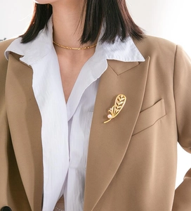 Détail d'une broche plume dorée avec zircons et perle rose sur une veste de costume