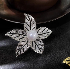 Détail macro d'une broche fleur à cinq pétales avec perle blanche et oxydes de zirconium